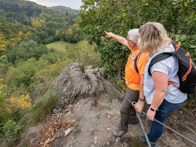 The picture shows a couple on a rock and a far-reaching view of the surrounding forests.