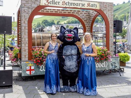Weinhoheiten Zell an der Mosel Auf dem Bild befindet sich das Maskotchen die Zeller Schwarze Katz. Links und rechts neben Ihr stehen die Weinhoheiten Laura und Johanna.