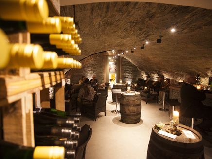 Wine tasting The picture shows a wine cellar with wine barrels set up as tables. The wine bottles are stored on the shelves.