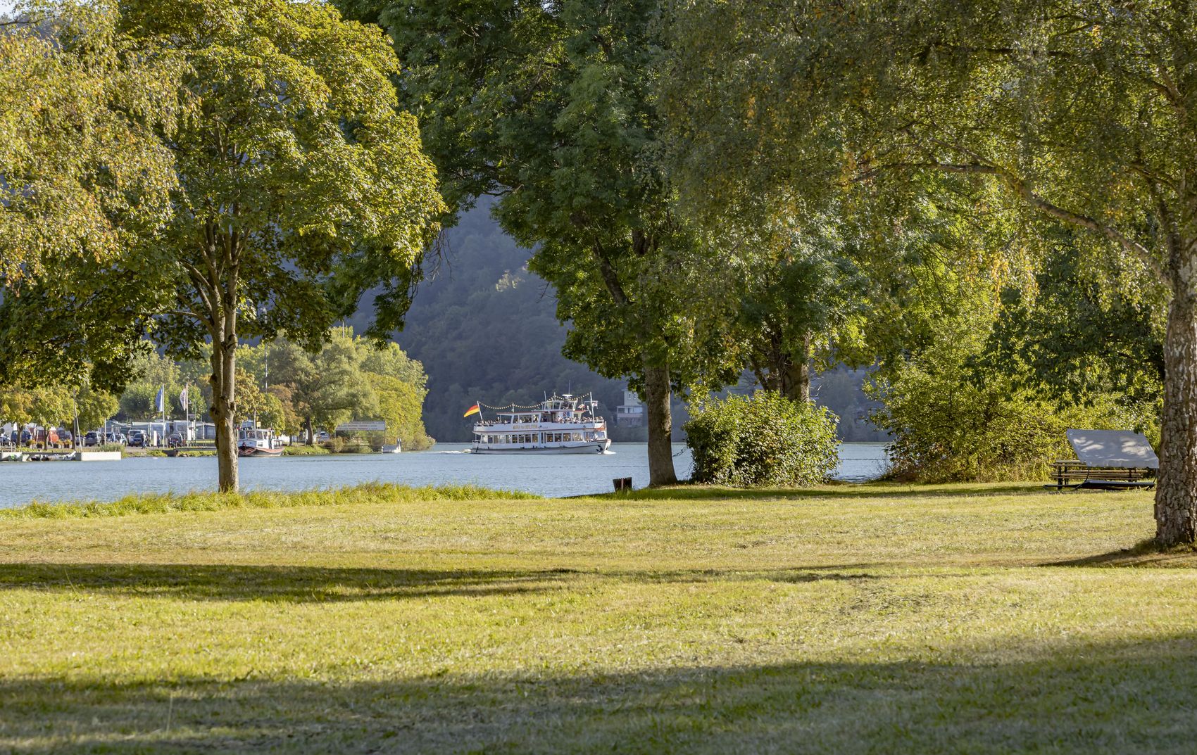 Schifffahrt Das Bild zeigt das Schiff Maria von Beilstein auf der Mosel zwischen Bullay und Alf. Im Vordergrund sind eine Wiese und mehere Bäume zu erkennen, da das Bild von dem Moselufer in Alf aufgenommen wurde. Im Hintergrund erkennt einen Wald sowie den Campingplatz von Bullay.
