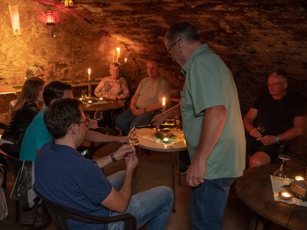 Lustige Kellerwanderung Auf dem Bild sieht man eine Gruppe von Gästen in einem Weinkeller wie sie mit einem Glas Wein anstoßen.