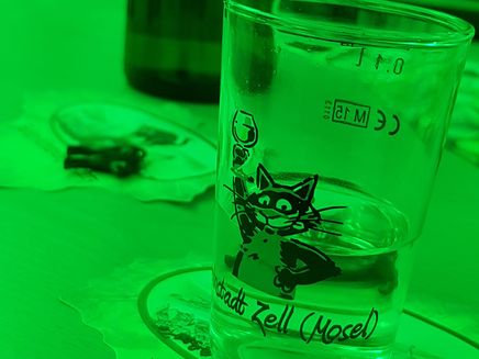 Light wine tasting The picture shows a jar with the Zeller Schwarze Katz on it. The picture was taken in green light. There is a wine bottle in the background.