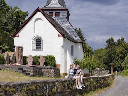 Neefer Petersberg light spot hiking trail The picture shows the Neef Petersberg Chapel with three young women sitting on the stone wall in front of the chapel.
