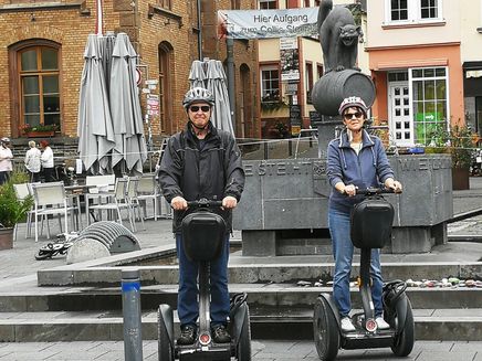 Segway fahren Auf dem Bild ist eine Frau und ein Mann auf Segways. Sie stehen vor dem Zeller Schwarze Katz Brunnen in Zell an der Mosel.