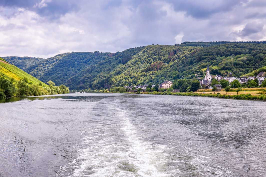 Schifffahrt Das Bild zeigt den Ausblick von einem Schiff auf Mosel bei dem Ort Briedel, welches sich links im Bild befindet. Im Hintergrund erkennt man Wälder.
