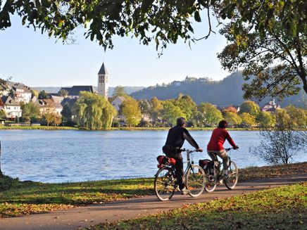 Radfahren Das Bild zeigt ein Paar beim Radfahren an der Mosel. Auf der anderen Moselseite ist der Ort Bullay zu erkennen.