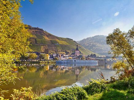 Shipping The picture shows a cruise ship on the Mosel in fine weather, standing in front of the town of Zell. In the background are St Peter's Church, the footbridge and the vineyards. The picture was taken from the banks of the mosel in Zell-Kaimt, so that sections of trees can be seen at the edge of the picture.