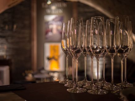 Wine bar Alte Stadtmauer The picture shows a row of sparkling wine glasses in the foreground. In the background you can see the logo of the winemaker.