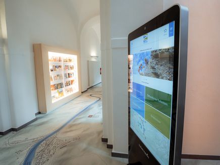Auf dem Bild befindet sich der Flur in der Tourist Information. Man erkennt den Fotoboden, die Touchstele und die Prospektwand.