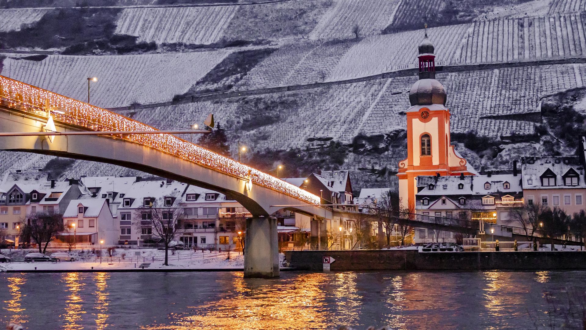 Zell (Mosel) bei Schnee Auf dem Bild befindet sich die Fußgängerbrücke in Zell an der Mosel am Abend. Sie ist beleuchtet und es liegt Schnee.