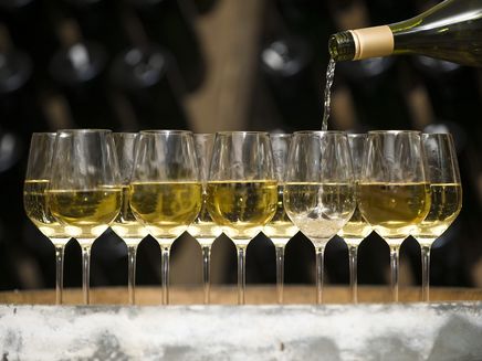 Wein Das Bild zeigt mehrere Weingläser, die gerade mit Wein befüllt werden.