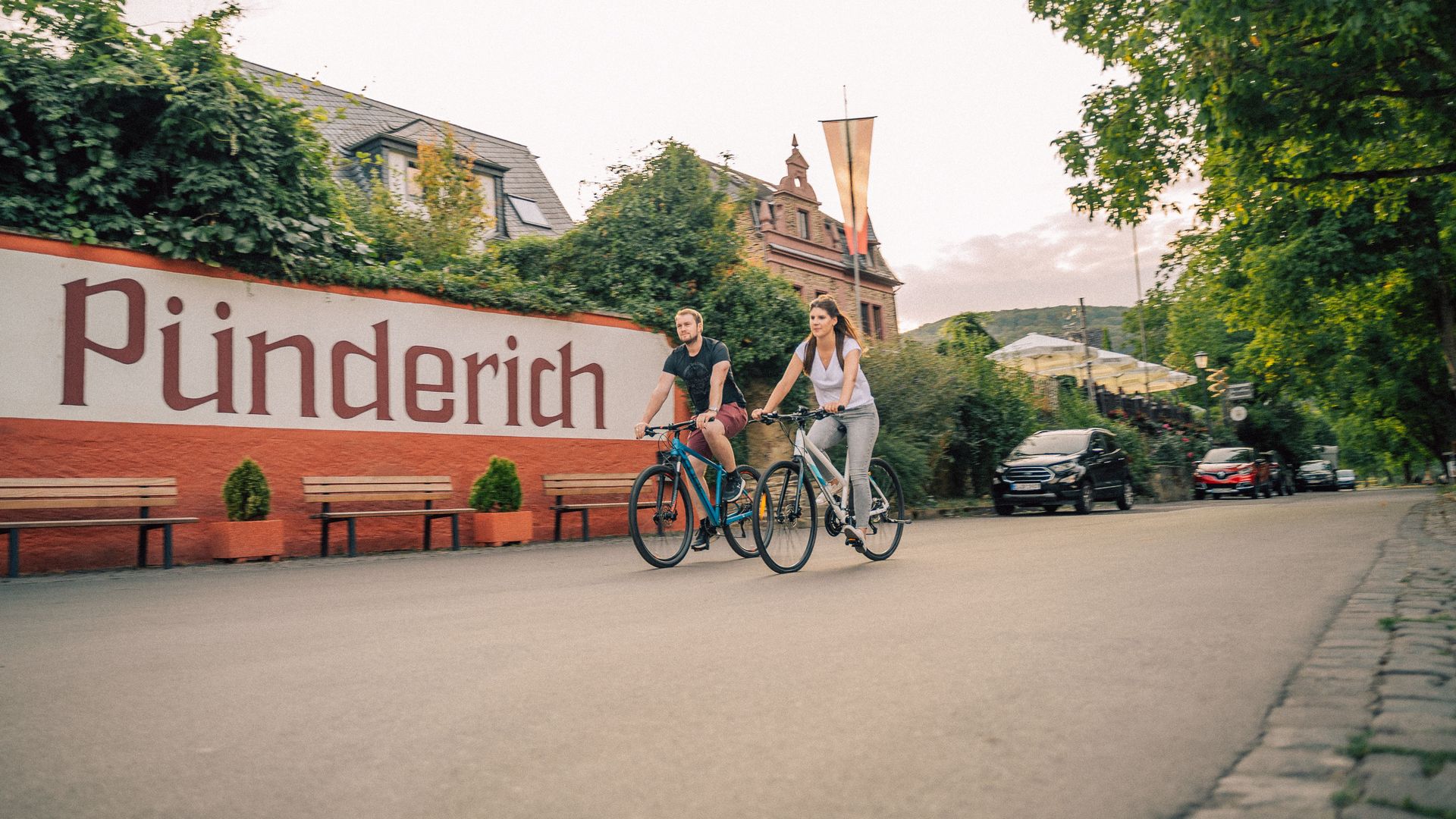 Auf dem Bild sieht man zwei Radfahrer die an der Moselpromenade von Pünderich entlang radeln.