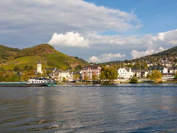 Das Bild ist von dem Fluss aus aufgenommen. Auf dem Bild befindet sich die Mosel, ein Schiff und der Ort Bullay.