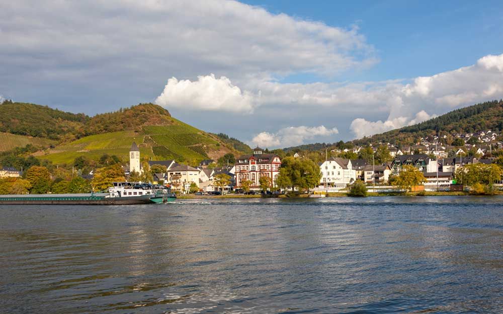 Ortsansicht Bullay Das Bild ist von dem Fluss aus aufgenommen. Auf dem Bild befindet sich die Mosel, ein Schiff und der Ort Bullay.
