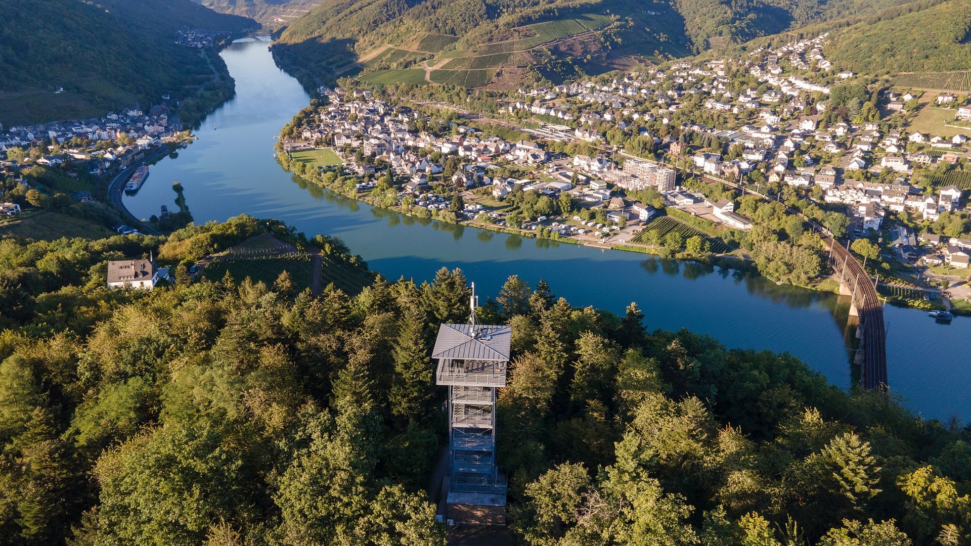 Prinzenkopfturm Umgeben von Bäumen befindet sich der Aussichtsturm Prinzenkopfturm. Dahiner befindet sich die Mosel die von der Doppelstockbrücke überkreuzt wird. Im Hintergrund liegt der Ort Bullay und links im Bild der Ort Alf.